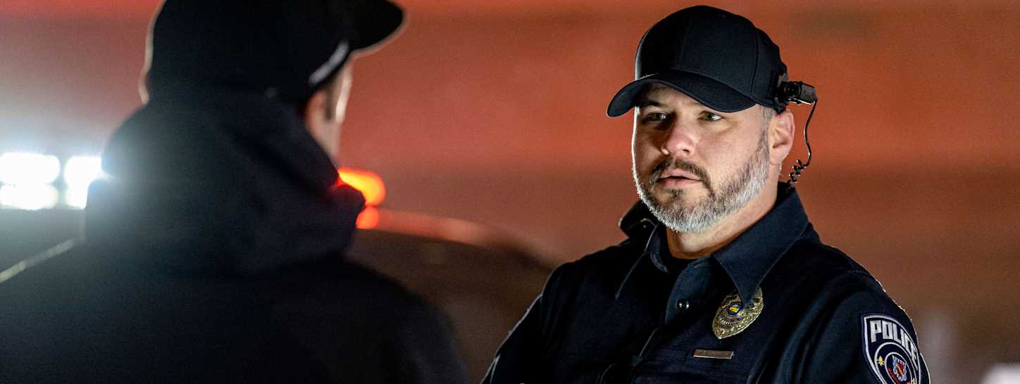 A well-equipped police officer questions a civilian as his body-worn camera records the interaction.